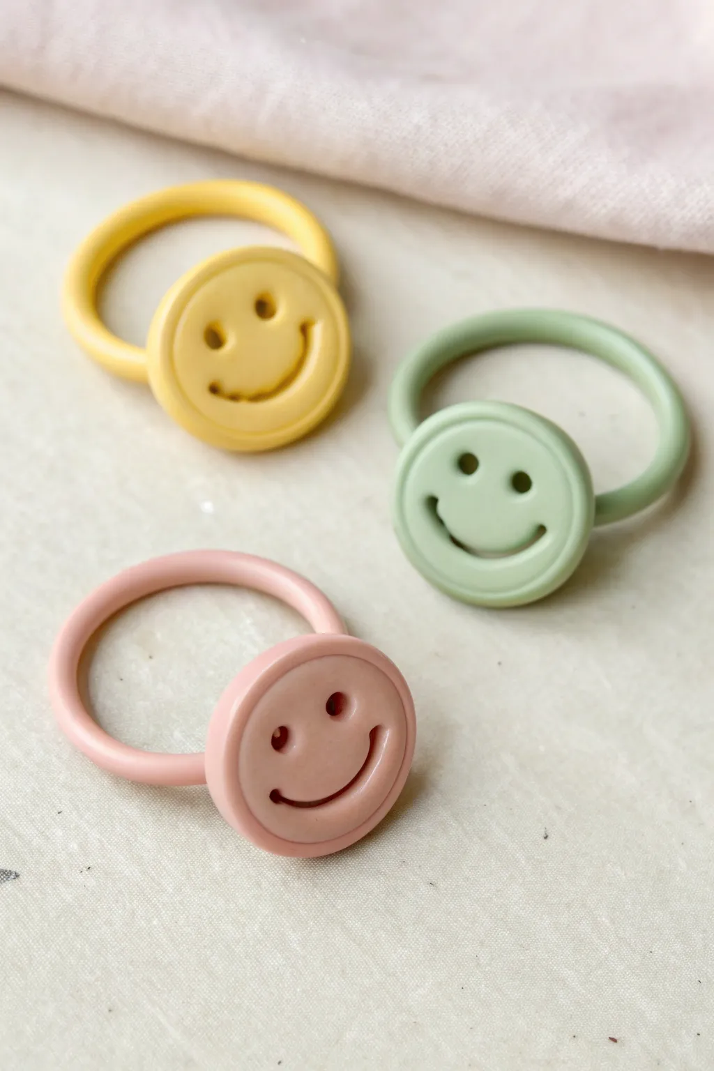 Minimal flat lay of smiley button rings in sunny yellow, blush, and sage for cheerful clay inspo.