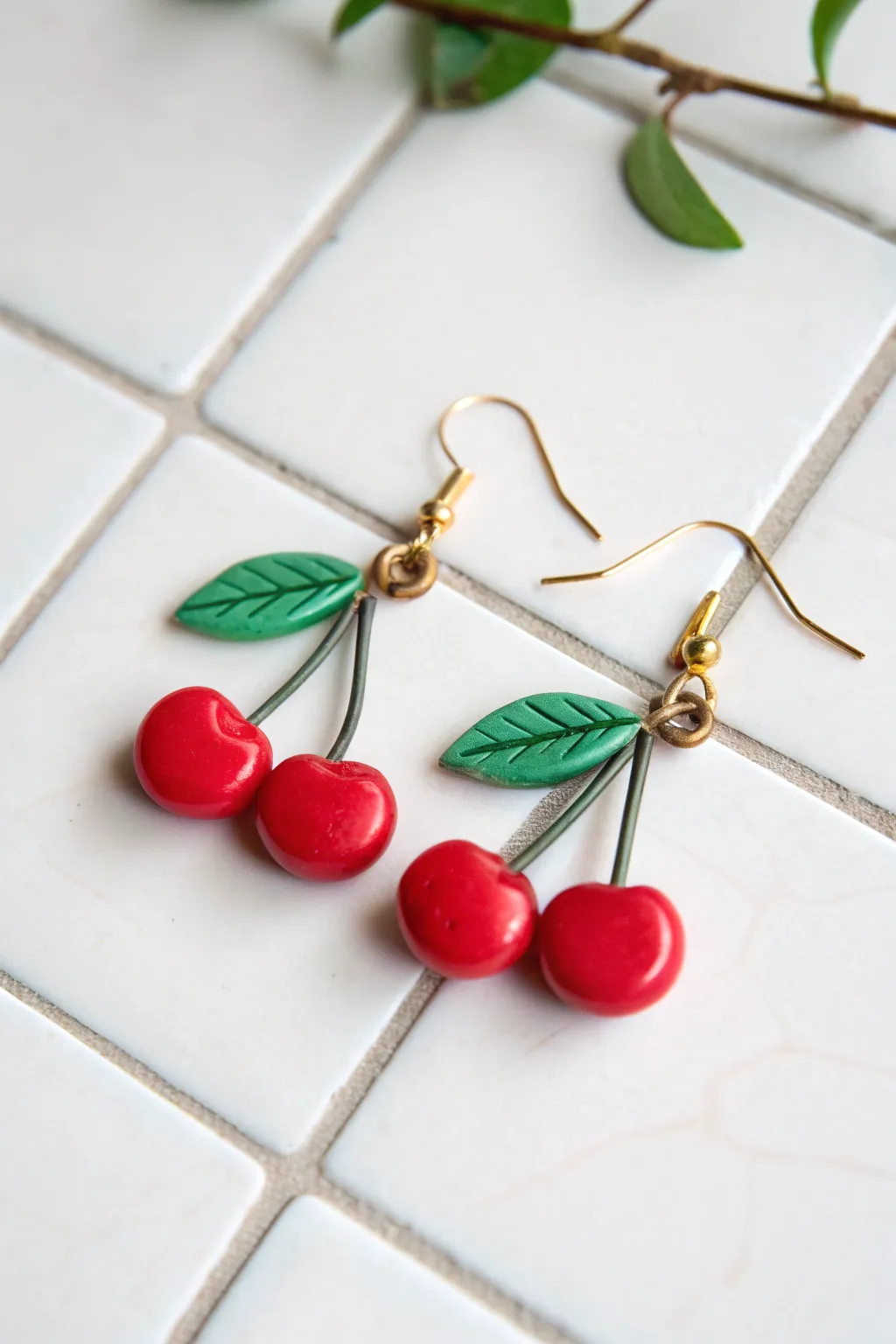 Glossy cherry cluster dangles in bright red with tiny green leaves on a clean stone backdrop