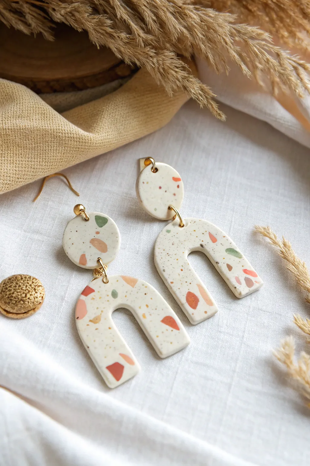 Terrazzo speckle arch earrings in soft pastels, minimalist flat lay with warm linen texture