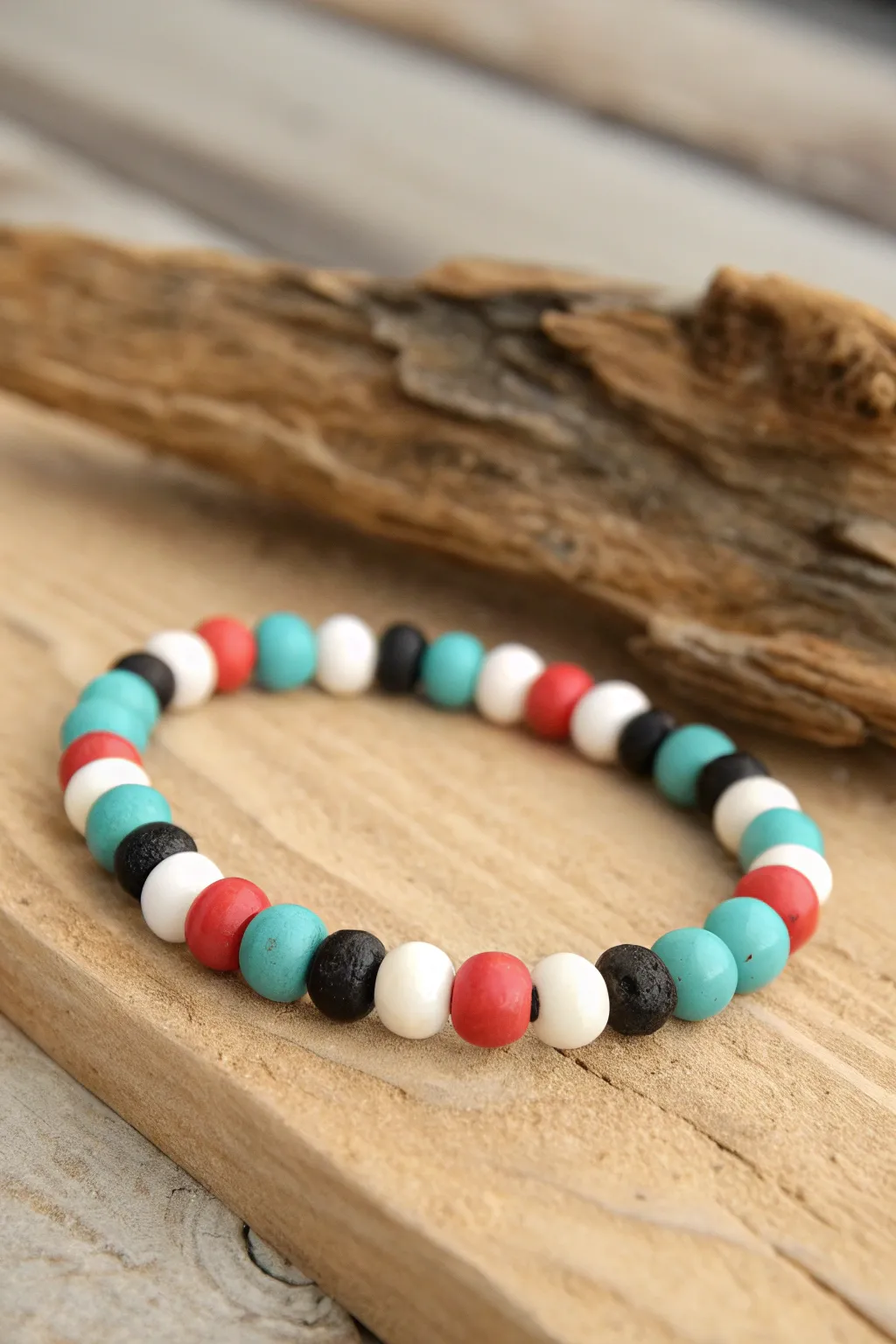 Four-color clay bead rhythm in turquoise, white, black, and coral on warm driftwood