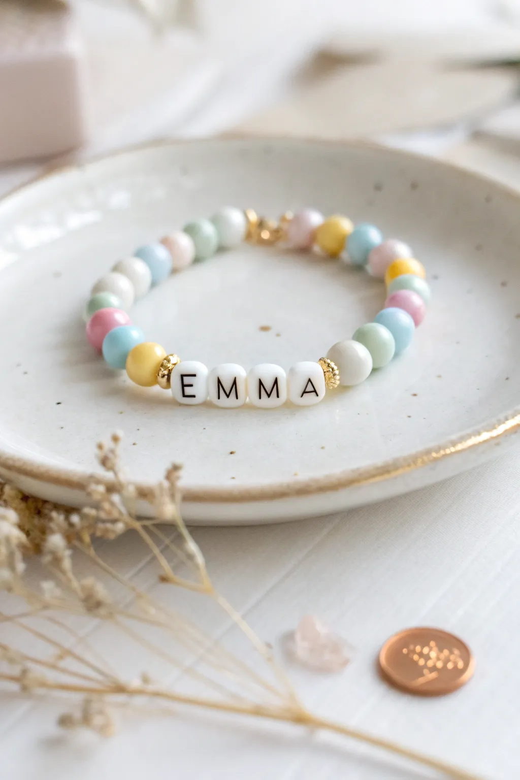 Preppy pastel clay bead name bracelet with gold spacers, styled minimalist on a white tray.