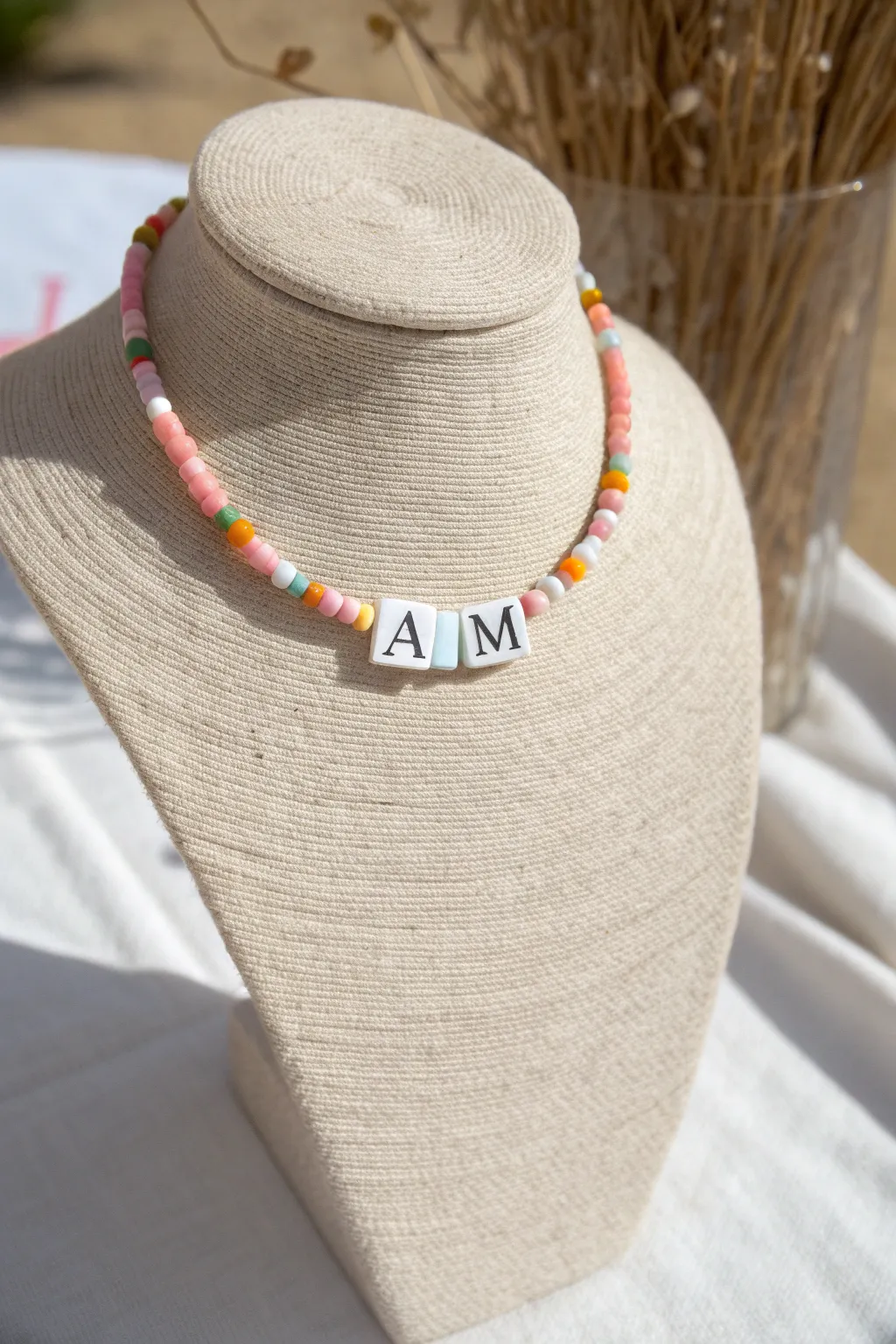 Bright preppy heishi necklace with centered initial beads, styled on a minimalist ceramic bust.