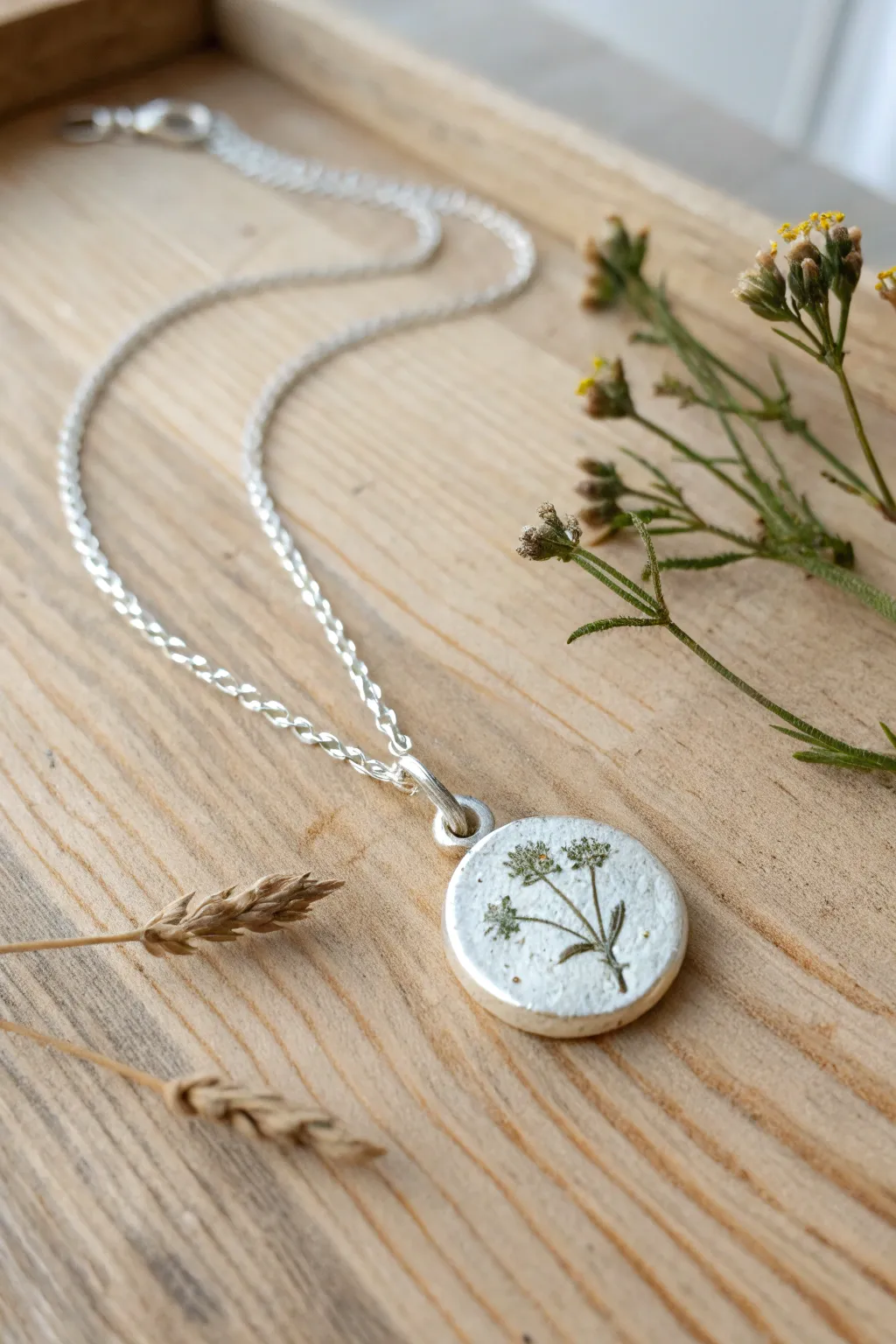 Pressed wildflower silver clay charm necklace styled on wood with a dried bloom, soft minimal boho.