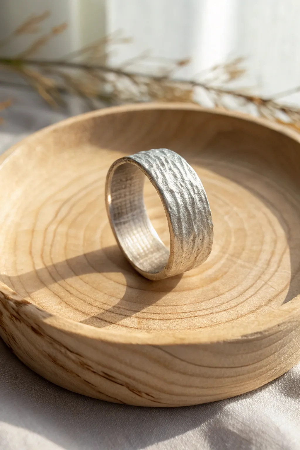 Organic bark-textured silver clay band on warm wood, minimal styling with crisp contrast.
