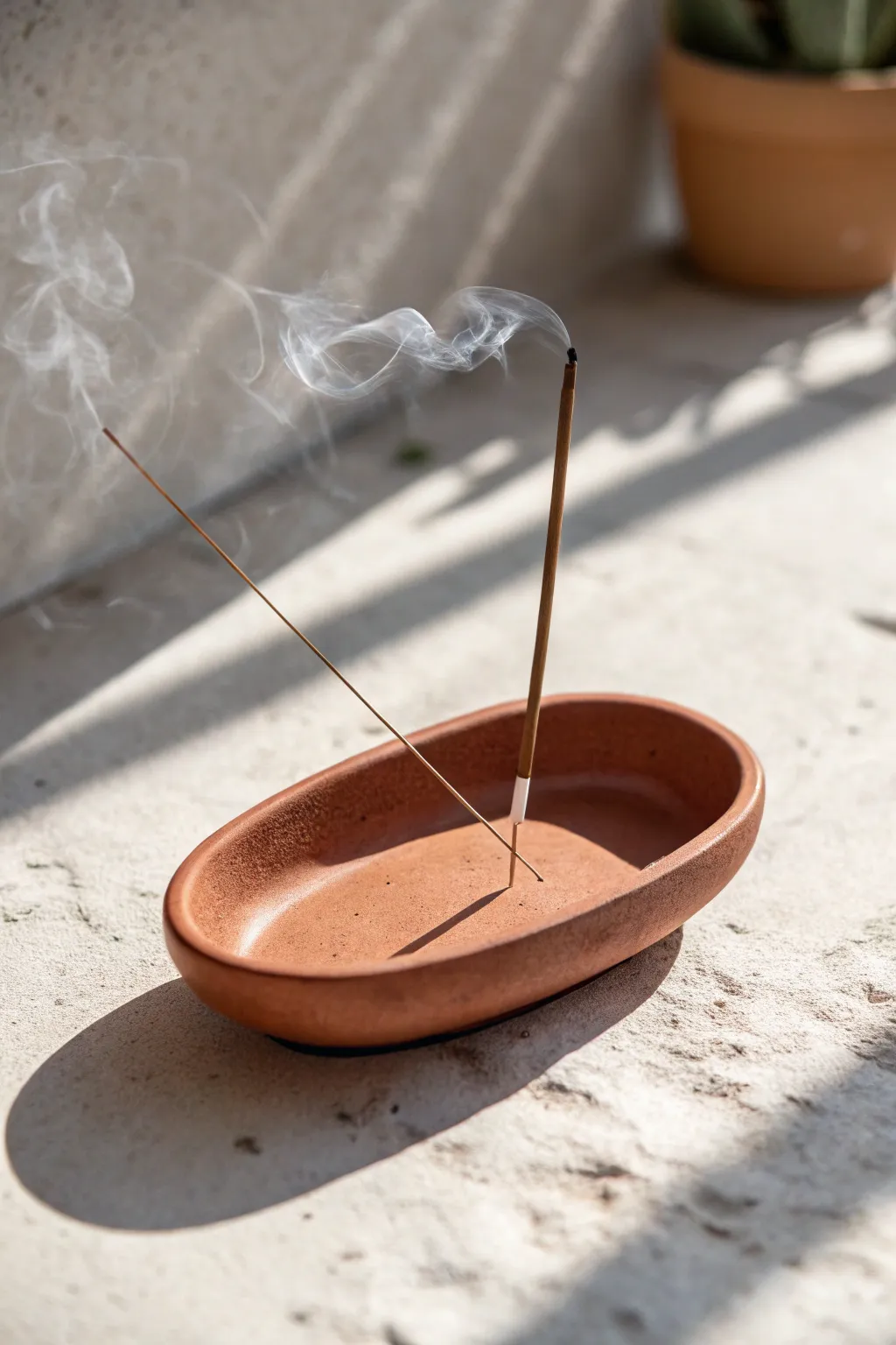 Minimal terracotta incense dish with a soft smoke wisp, styled on pale stone for calm contrast.