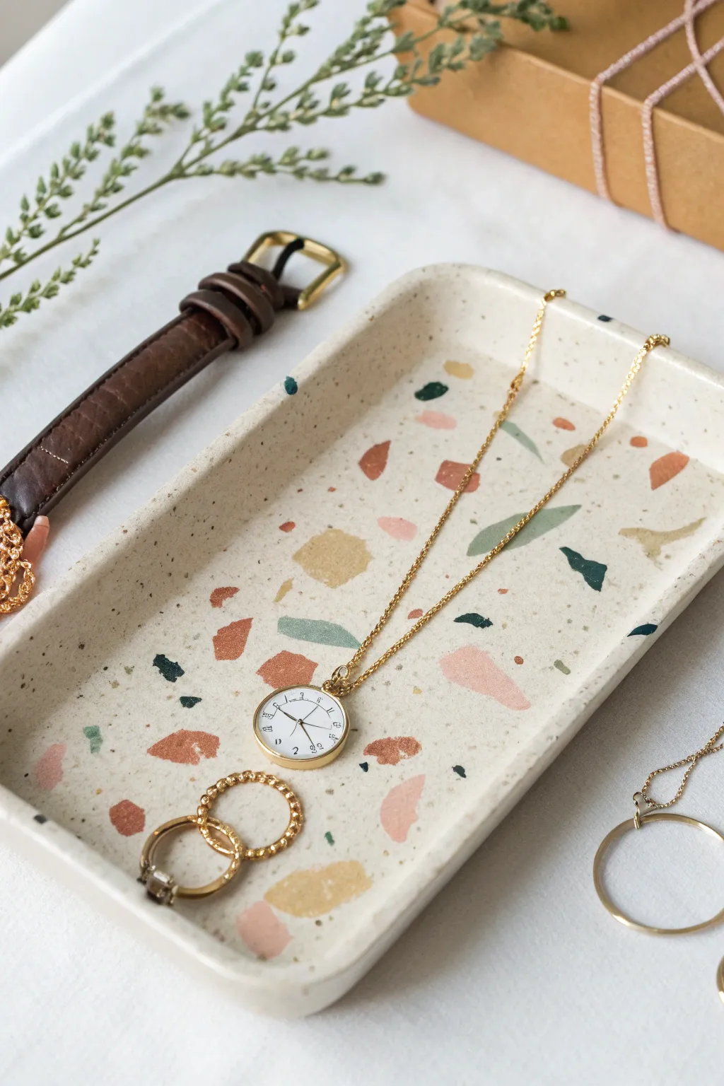 Terrazzo-style air dry clay jewelry tray with soft flecks, styled simply with necklaces and a watch.