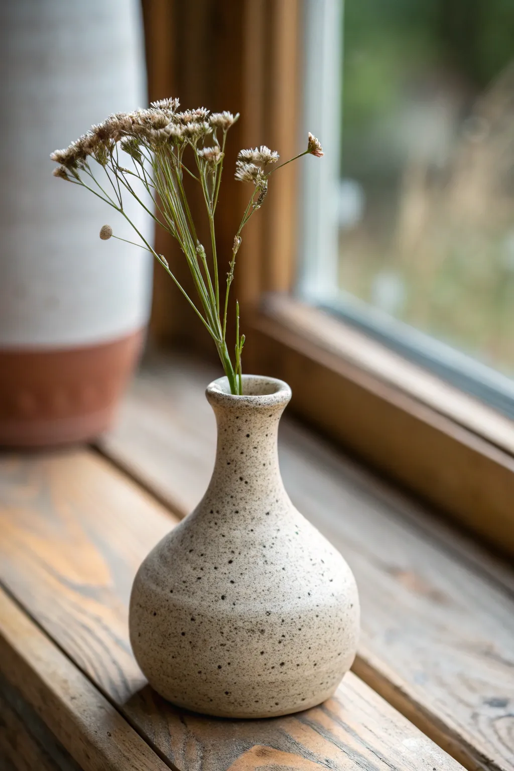 A tiny off-center bud vase in warm clay tones, styled minimally with one wildflower stem.