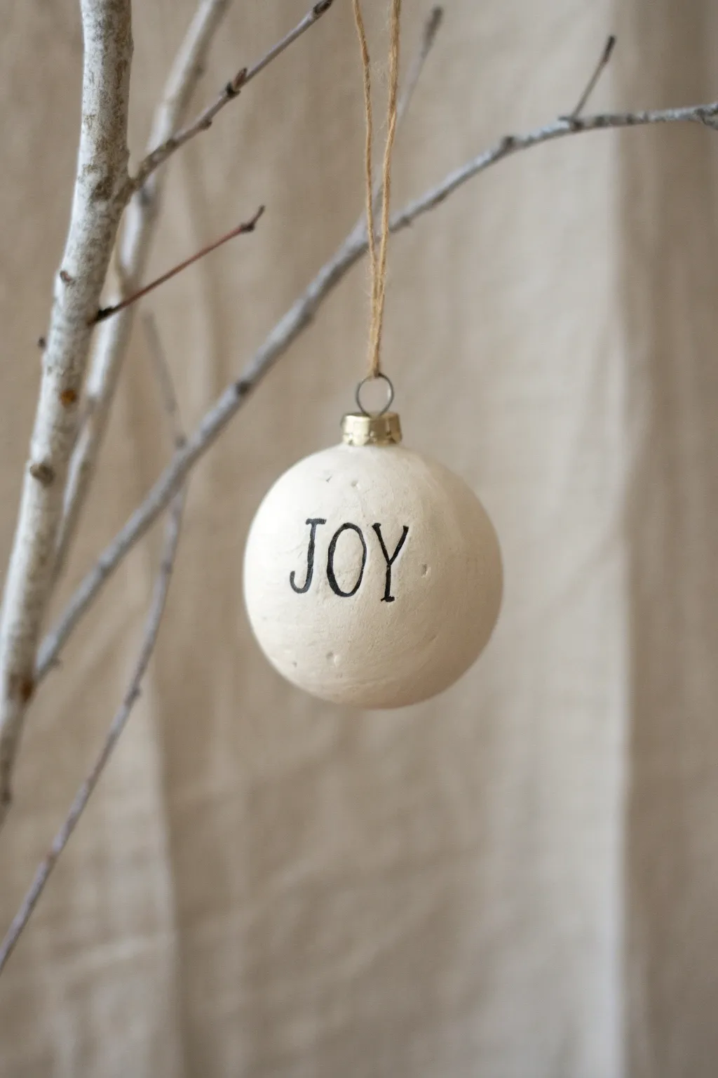 Simple air dry clay ornament with handwritten holiday word, hung from a natural branch.