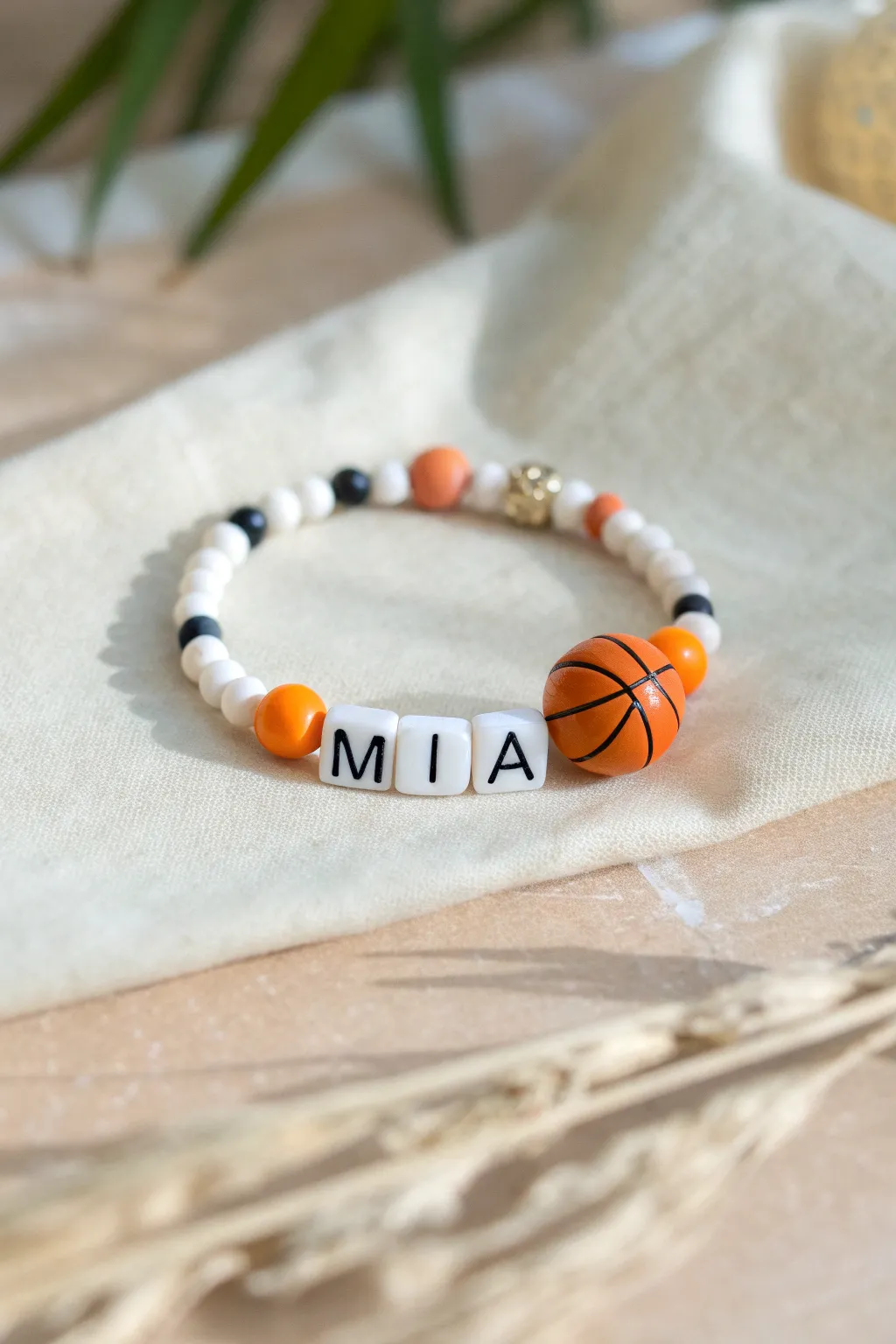 Personalized clay bead bracelet with name beads and a tiny basketball, styled in minimal Scandi tones.