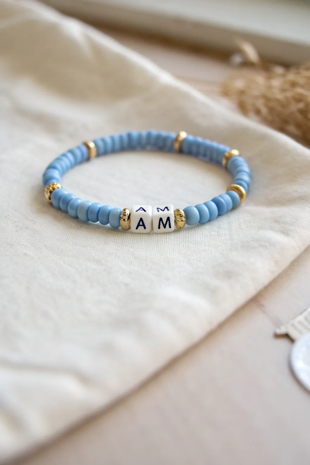 Blue heishi clay bracelet with white initial beads and gold spacers, calm Scandinavian boho style.