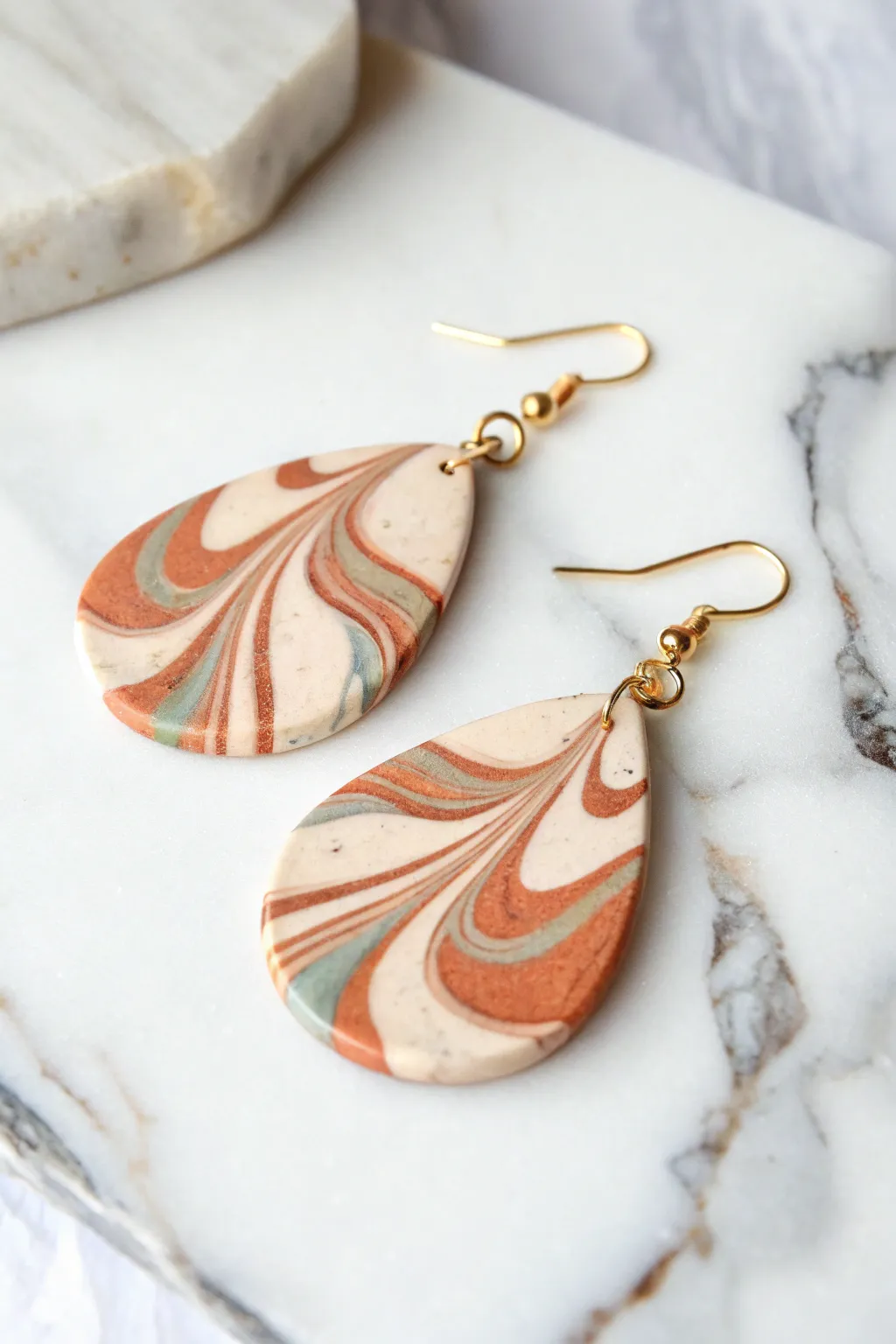 Marbled swirl drop earrings in terracotta, ivory, and sage on a clean stone backdrop