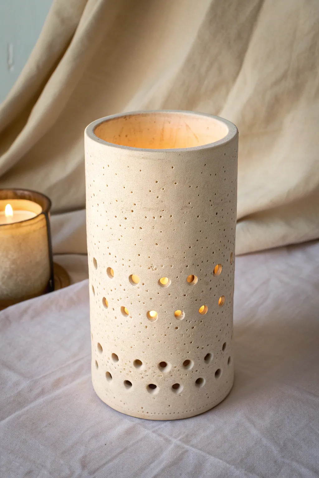 Soft speckled clay luminary with hole gradient, glowing warmly from tiny to bold cutouts