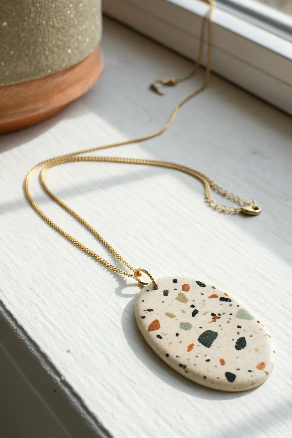 Terrazzo speckled clay pendant necklace in soft neutral tones, minimal flat lay with contrast