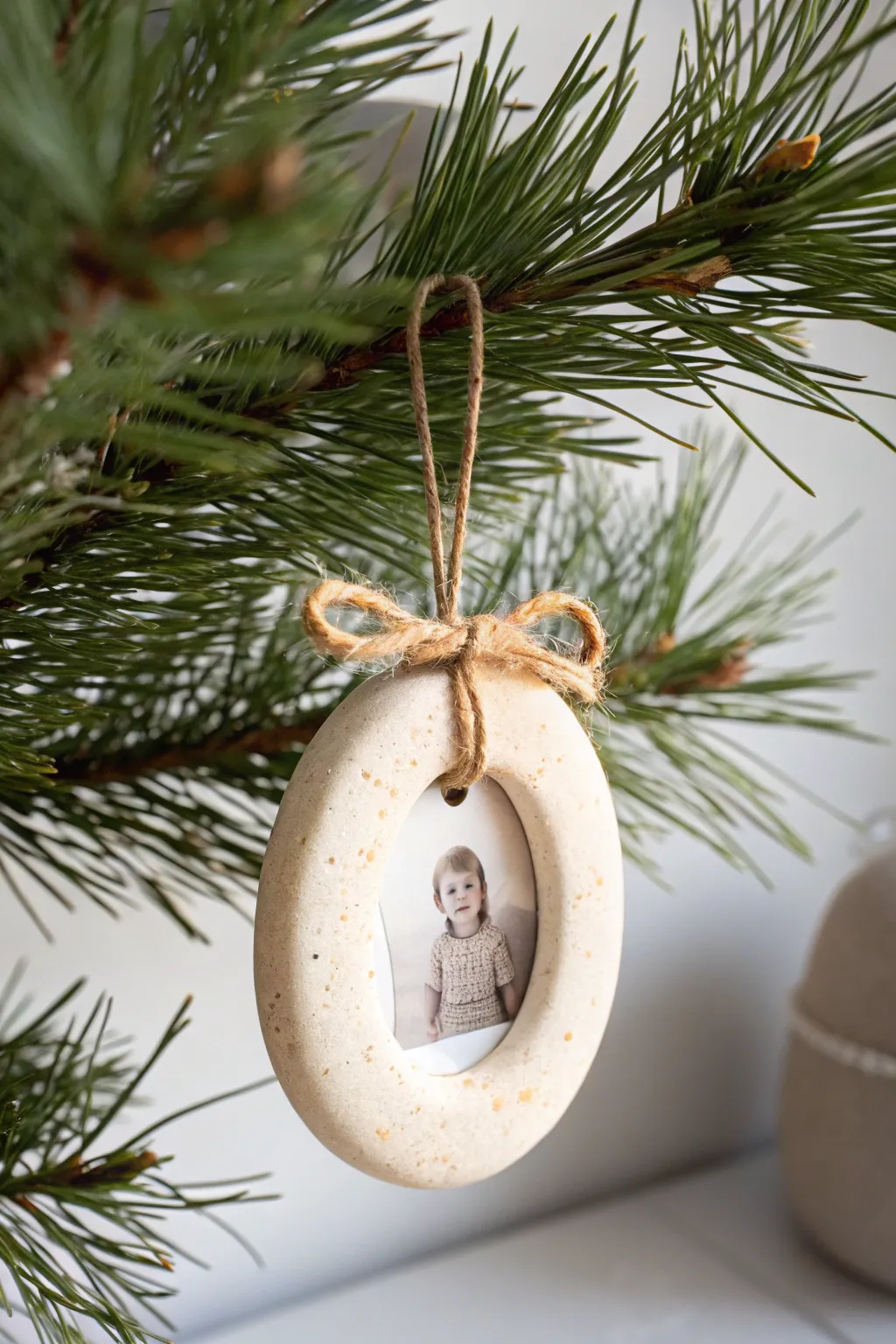 Simple clay photo frame ornament with a tiny portrait, hanging from a pine branch, cozy and timeless