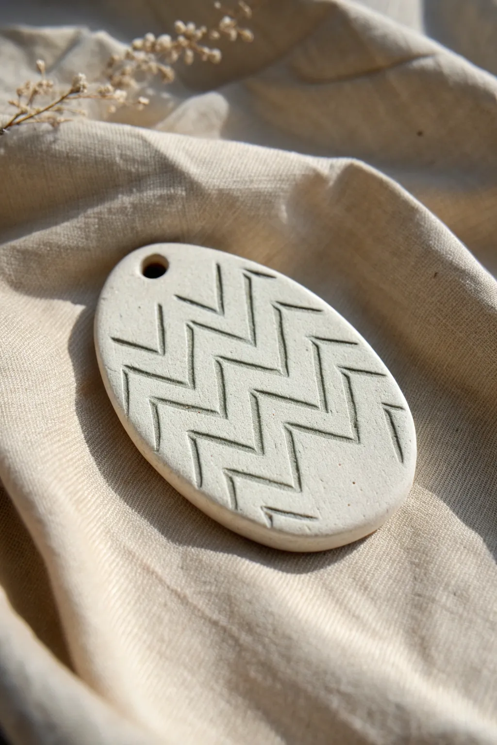 Minimal chevron-carved clay tag with soft contrasting inlay, styled on linen for pattern ideas.