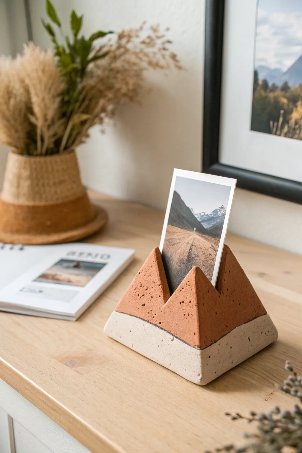Minimal mountain ridge clay photo stand holding an instant photo on light wood, soft shadows.