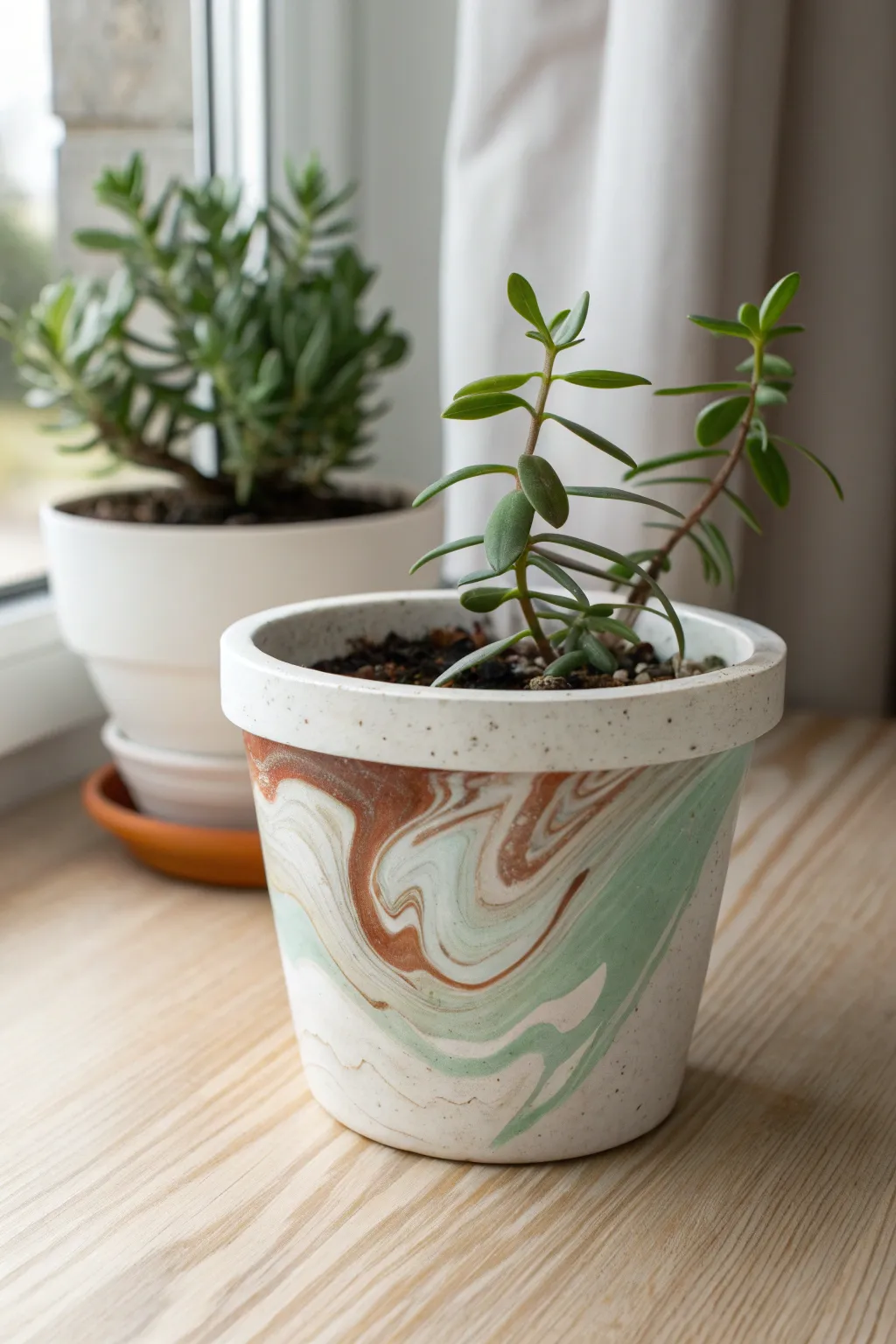 Marbled paint-pour clay pot in creamy white with sage and terracotta swirls, styled simply.