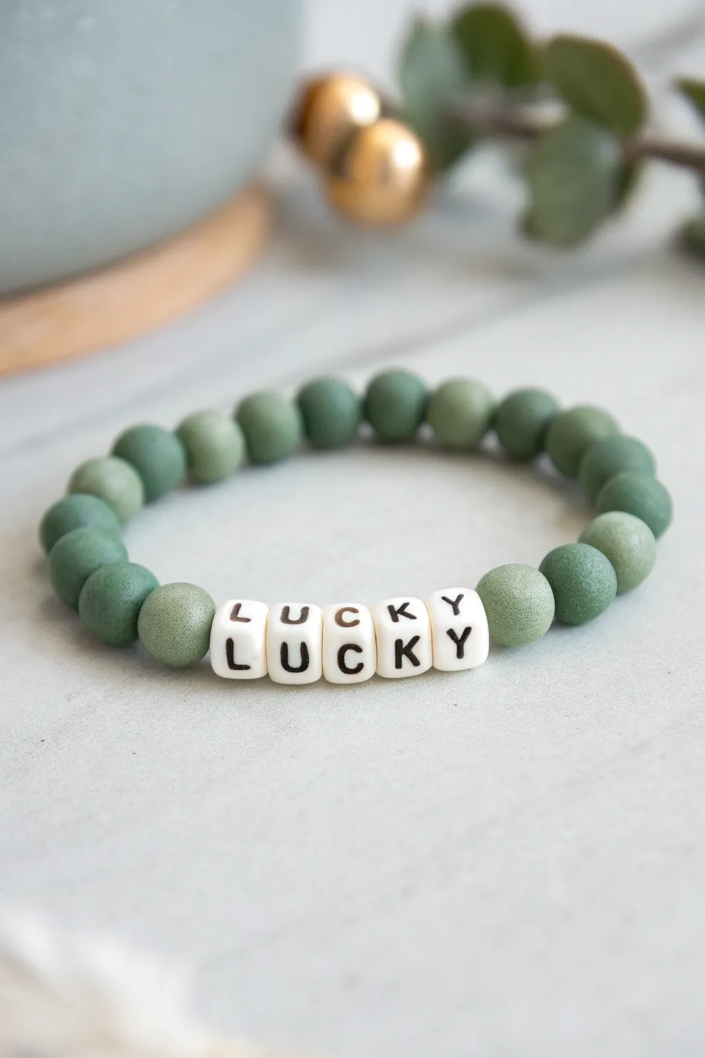 Minimal green clay bead bracelet with white letter beads spelling LUCKY on a pale gray backdrop