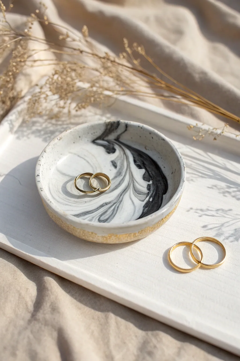 Minimal marble-drizzle trinket dish in liquid clay, styled with a few rings on soft linen.