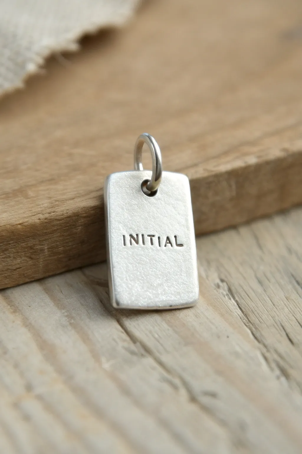 Minimal metal clay initial tag pendant on raw wood, a simple stamped keepsake for beginners