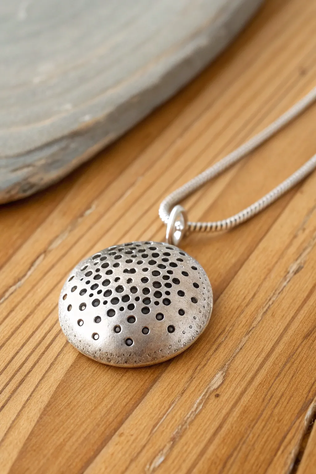 Seed pod texture silver clay pendant on warm wood, minimalist boho style with handmade contrast