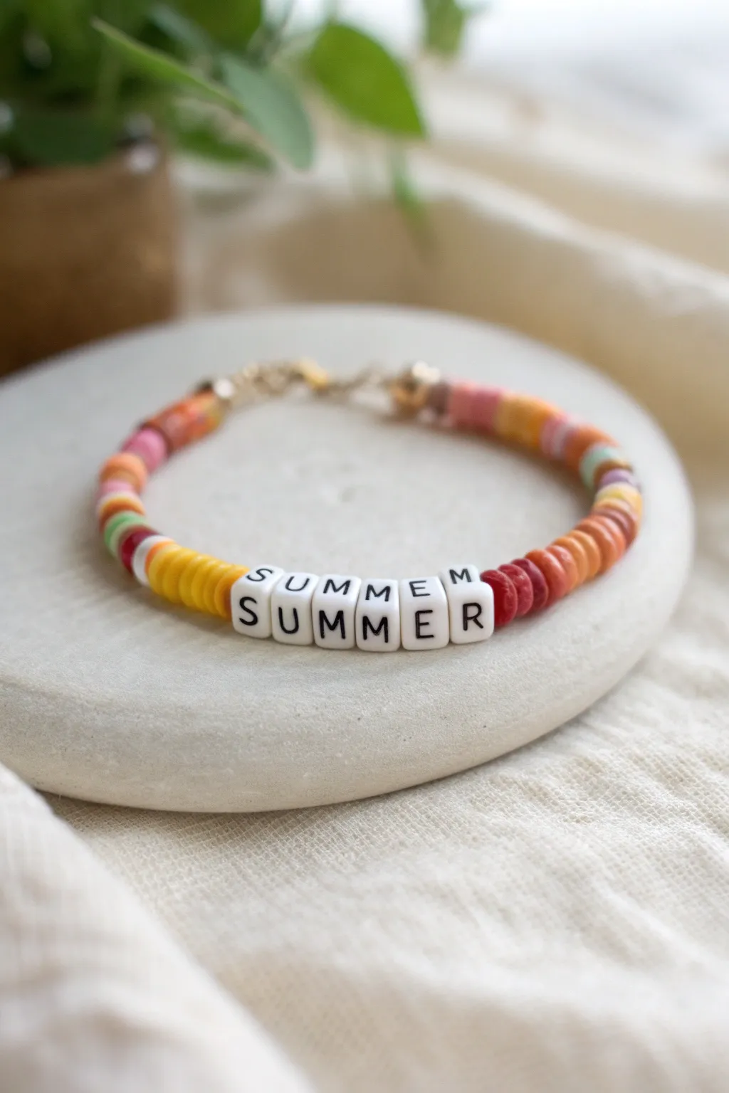 Sunset-toned clay bead bracelet with SUMMER letter centerpiece, styled minimalist on linen