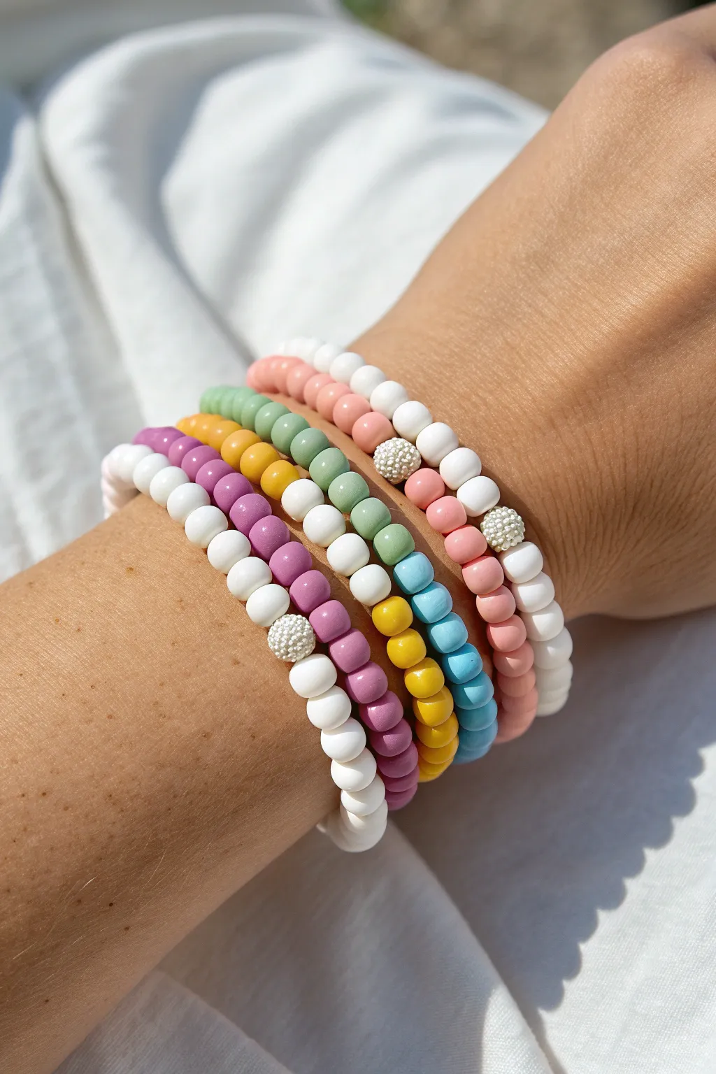 Sunlit rainbow clay bead stack with crisp white spacers for fresh, playful summer vibes.