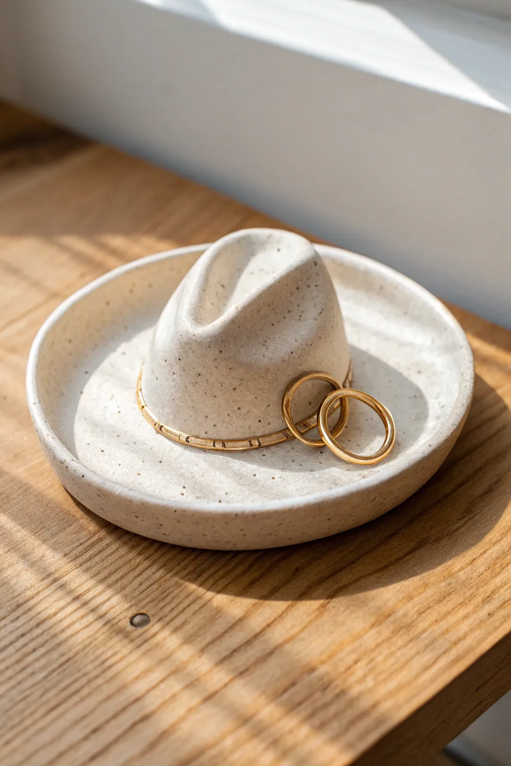 Speckled cream cowboy hat ring dish with a warm minimalist vibe, holding a pair of rings.