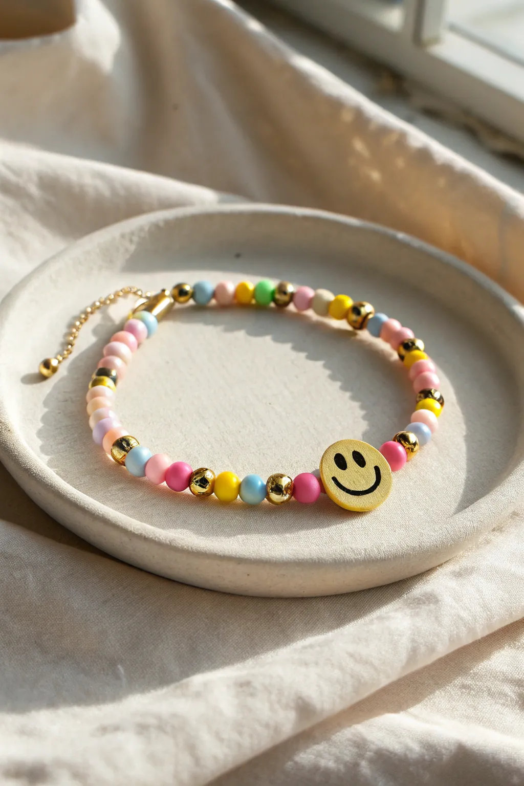 Playful clay bead bracelet with a simple smiley focal and gold spacers in warm sun.