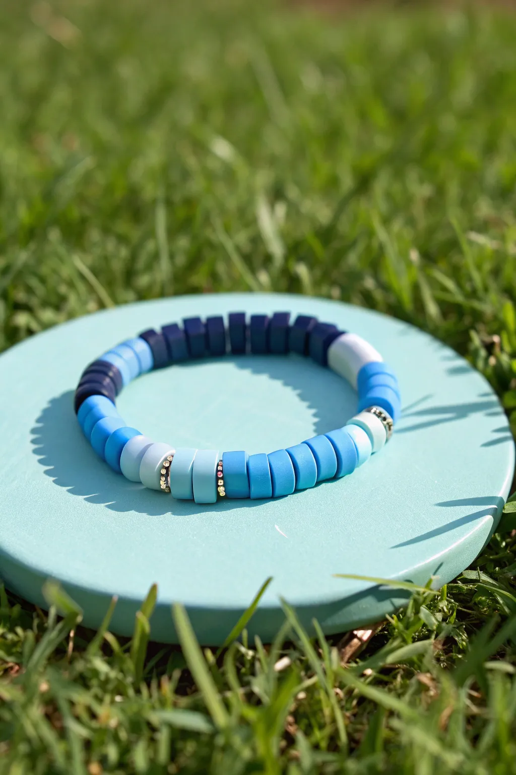 Tri-tone blue clay disc bracelet on bright green grass, bold color blocking with a clean finish