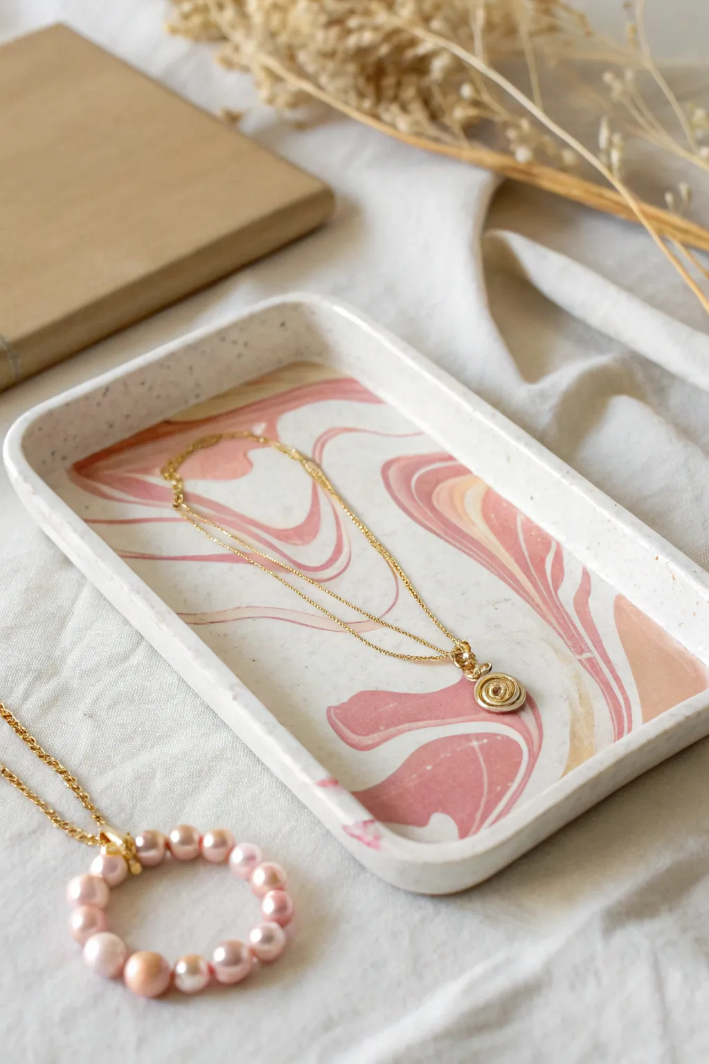 Blush and cream swirl jewelry tray with a draped gold necklace, minimalist and softly boho.