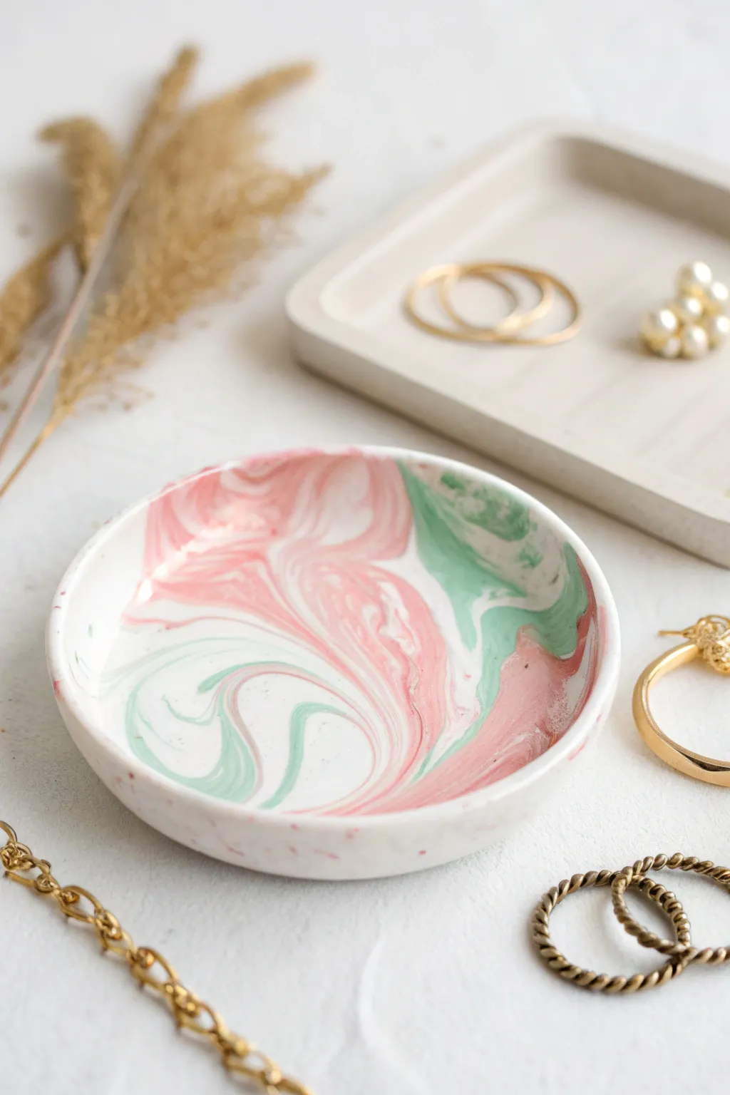 Glossy marbled air dry clay dish with soft color swirls, styled simply with gold jewelry
