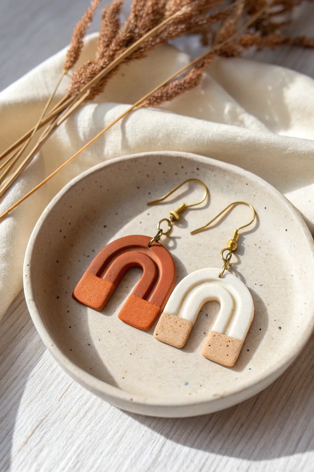 Minimal two-tone polymer clay arch earrings on a simple dish, perfect for beginner makers.