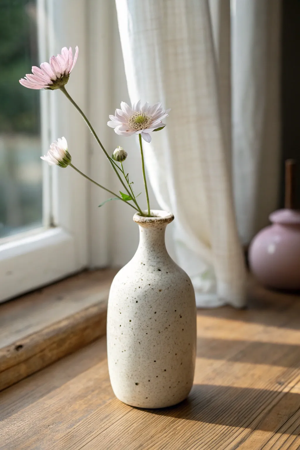 Tiny handmade bud vase in soft clay tones, sunlit and serene with one delicate stem.