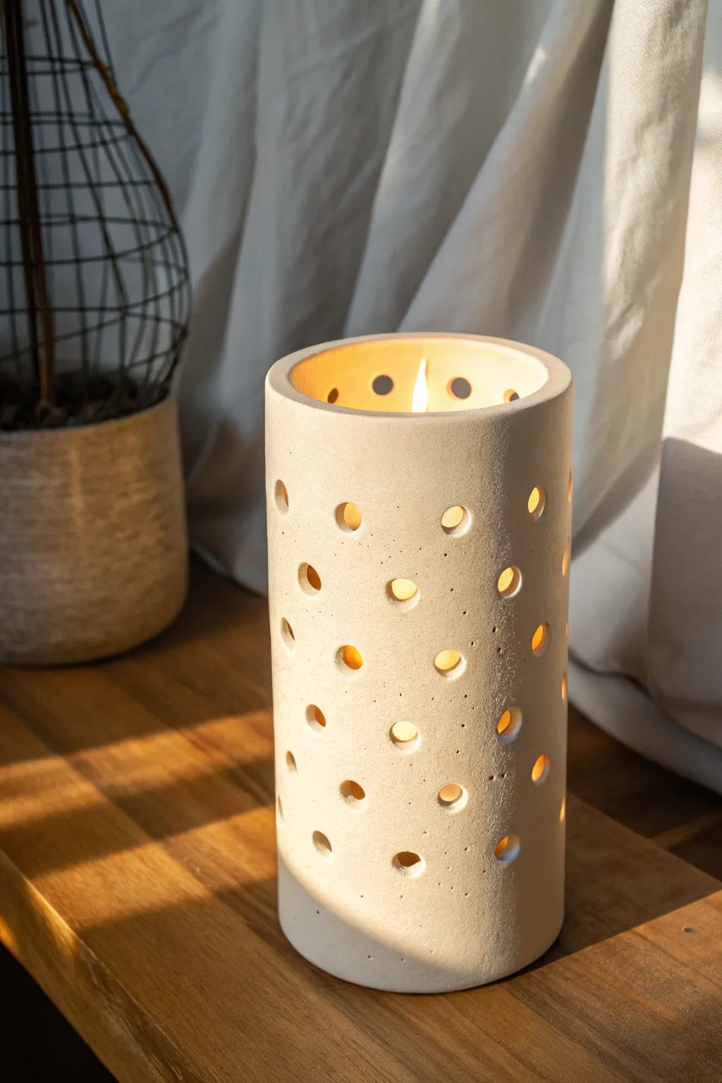 Minimal hollow clay luminary with punched holes, softly glowing in a cozy Scandinavian corner