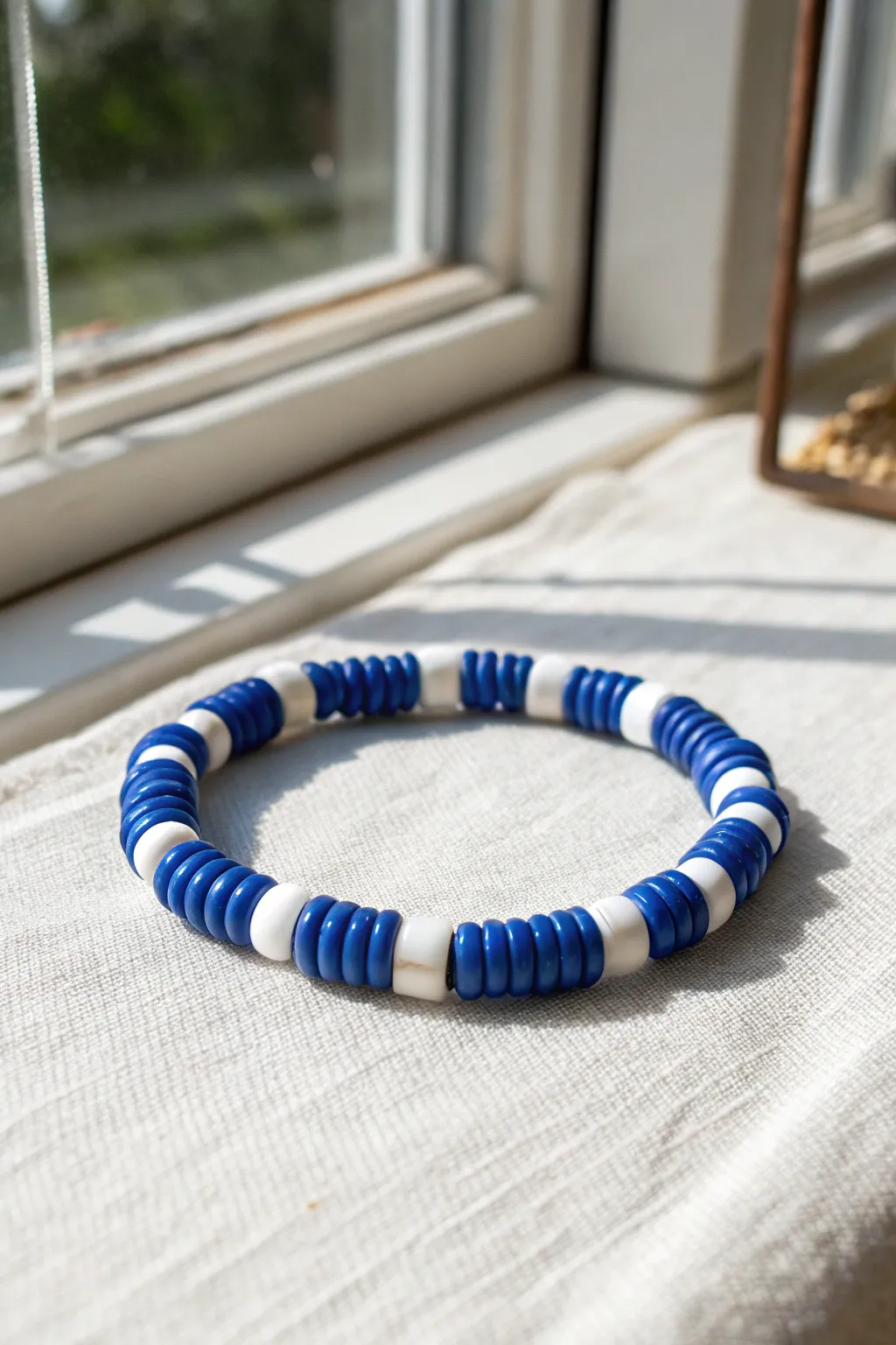 Preppy blue and white clay bead bracelet with clean nautical stripes on a crisp linen backdrop.