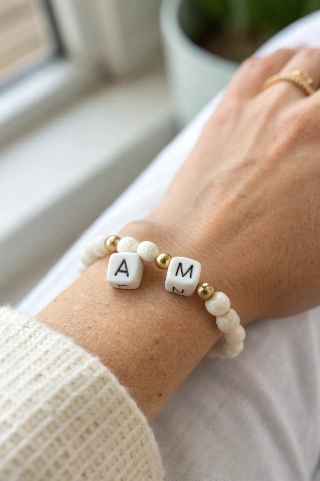 Preppy initial bead bracelet with white clay discs and gold accents, styled in a clean wrist stack.