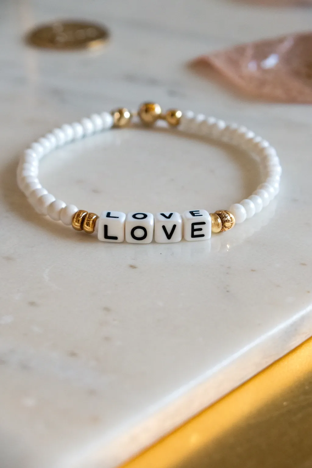 Cute preppy motto bracelet: white heishi, LOVE letter beads, and delicate gold spacers on a clean flat lay.