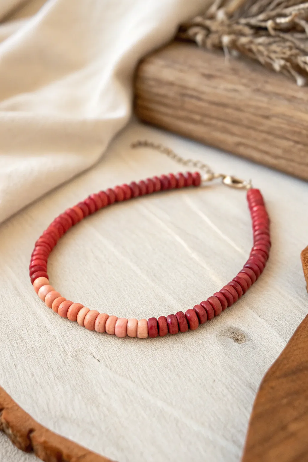 A single clay heishi bracelet in a smooth red ombre, from deep brick to soft coral.