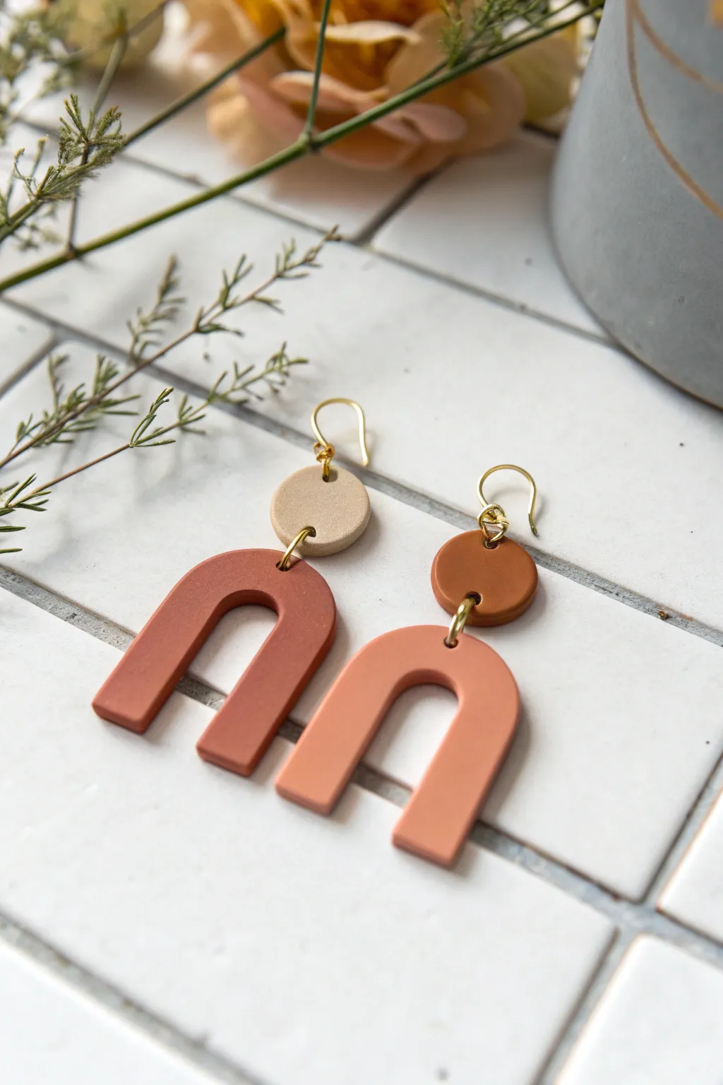 Flat-cut polymer clay arches in muted tones on white tile, minimalist boho earring inspo.