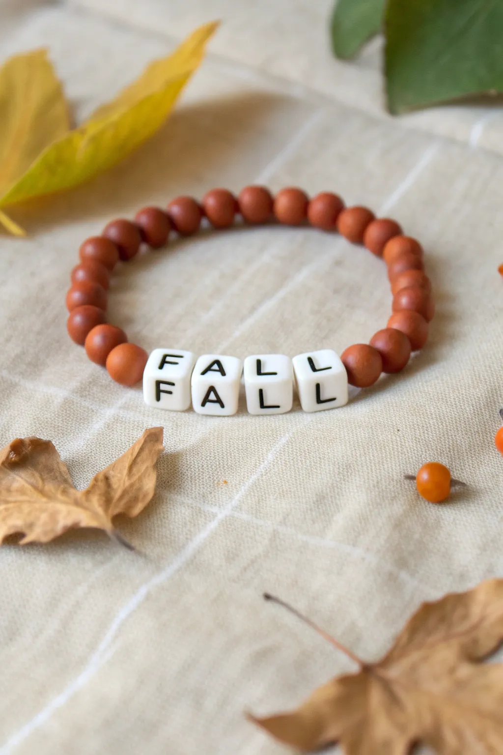 Minimal fall bracelet with FALL letter beads, burnt orange and cream clay beads on linen.