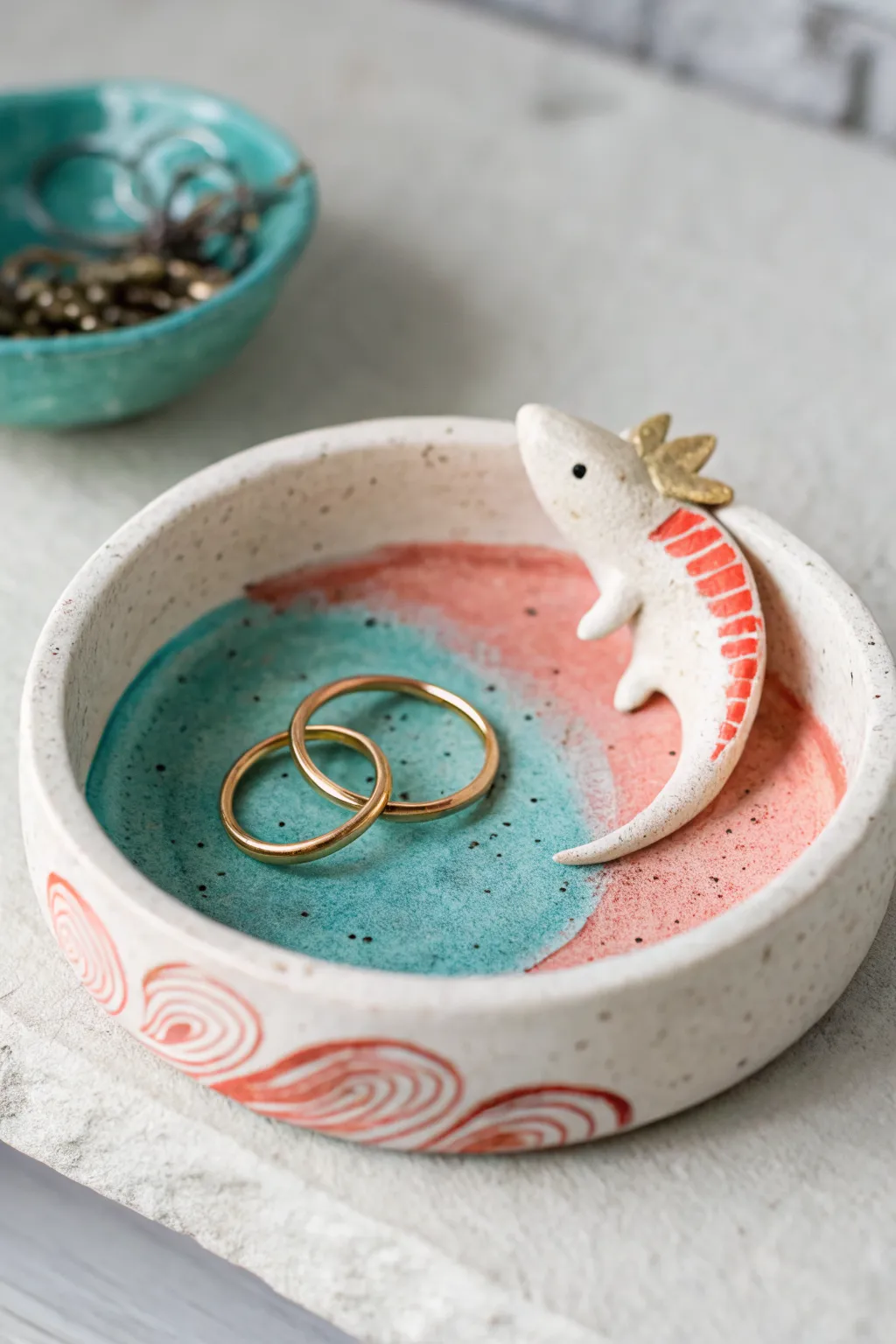 Axolotl ring dish with curled tail rim, bold glaze, and two simple rings for scale.