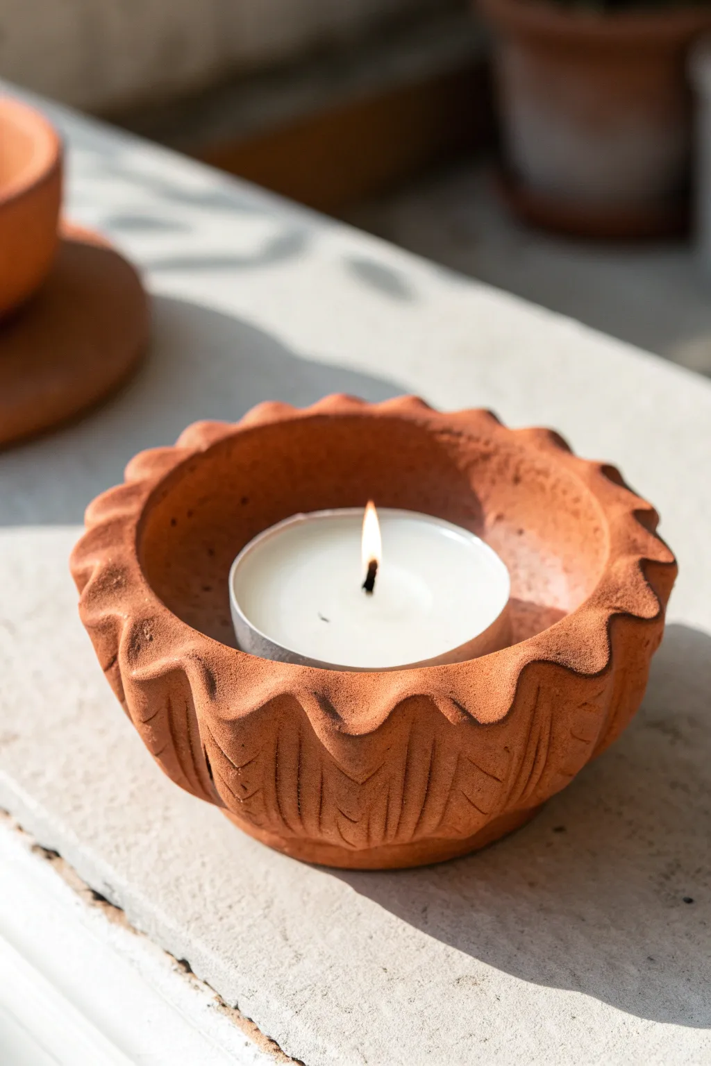 Minimal wavy clay tea light holder in bold terracotta, softly lit for cozy Scandinavian calm
