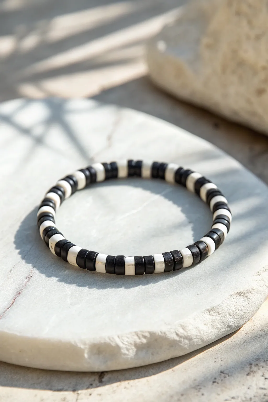Monochrome heishi bracelet in a checker mix, bold black and white blocks on pale stone.