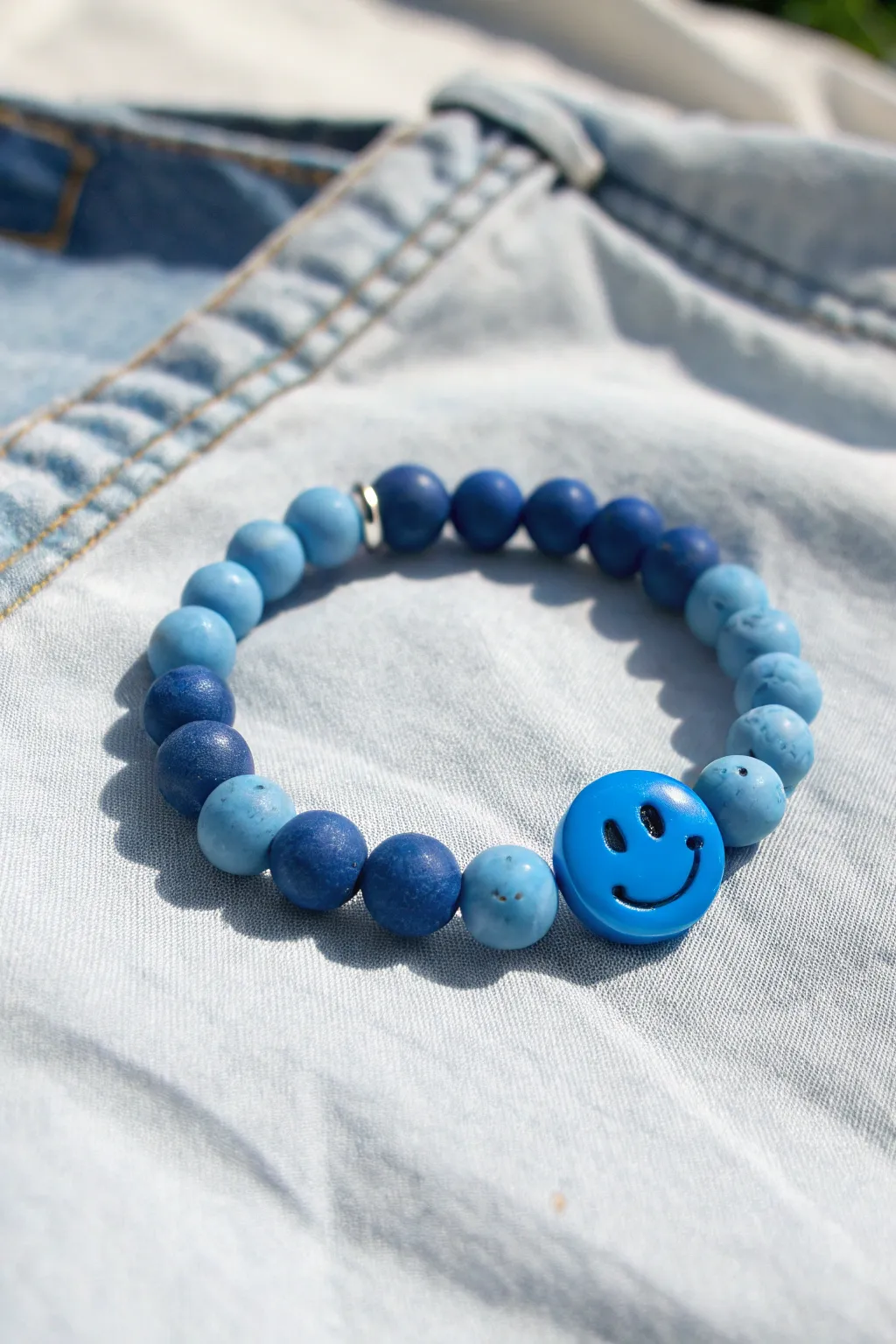 Cheerful blue clay bead bracelet with smiley focal beads, styled on light denim in soft daylight
