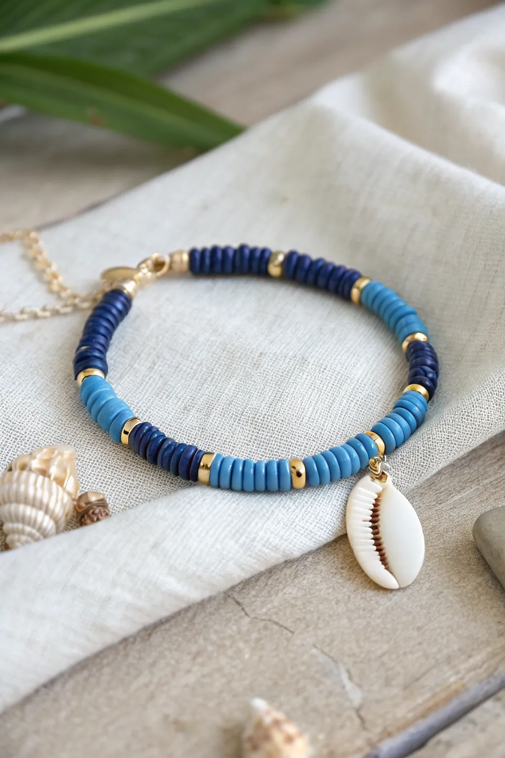 Beachy blue heishi bracelet stack with a cowrie shell charm, styled minimal on warm linen.