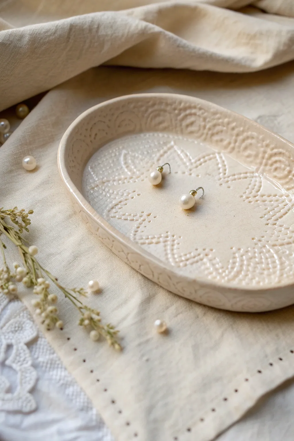Lace-imprint clay jewelry tray in soft ivory, styled on linen with pearl studs for vintage charm.