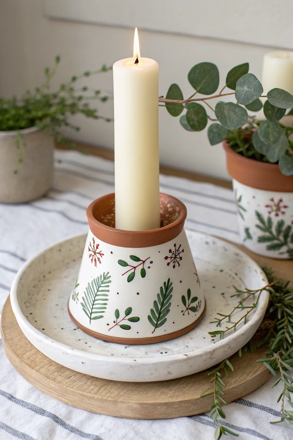 Cozy inverted clay pot candle pedestal with subtle holly paint, perfect minimalist Christmas centerpiece.