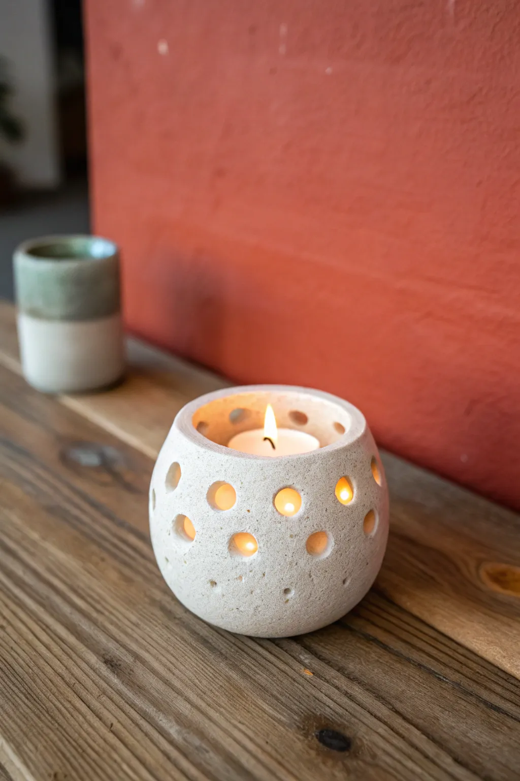 Simple clay tea light holder with easy cutouts, glowing warmly on wood in minimalist style