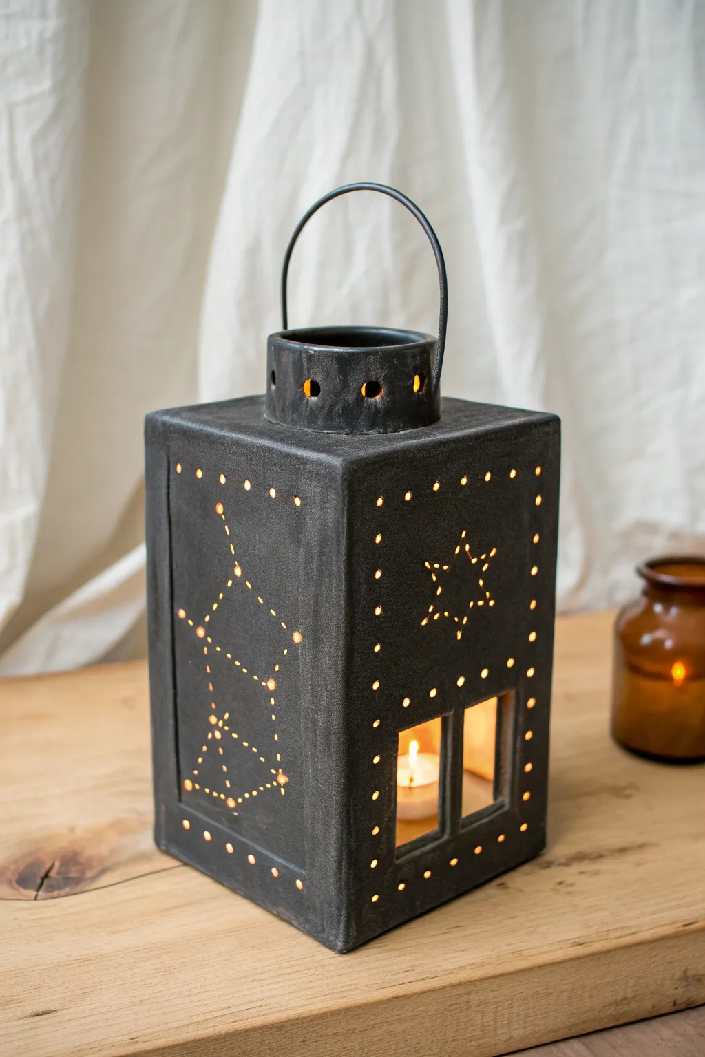 Charcoal slab lantern with dot-pierced constellations, casting a warm night-sky glow.
